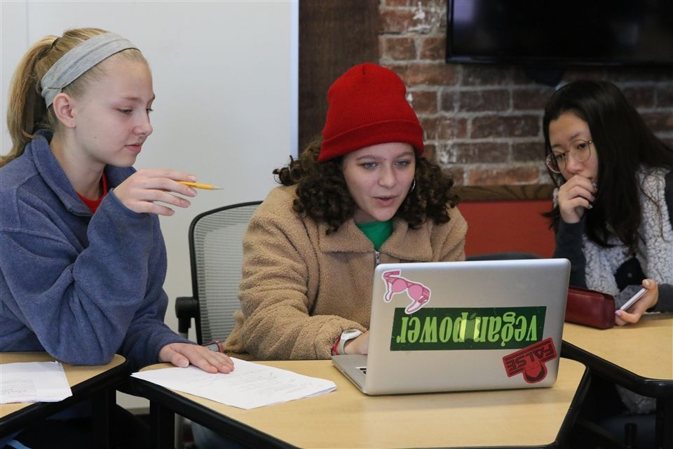 Three students in class working on a small group project with a laptop.